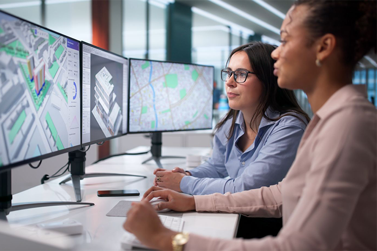 two woman looking a 3 computer screens