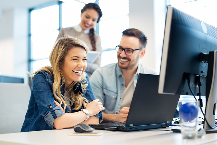 team smiling in a office facing a computer monitor