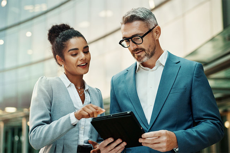 profession woman and man looking at tablet outside urban building